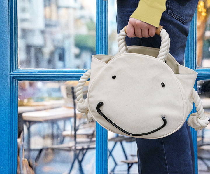 フェイスモチーフのキナリ色のトートバッグを持っている人